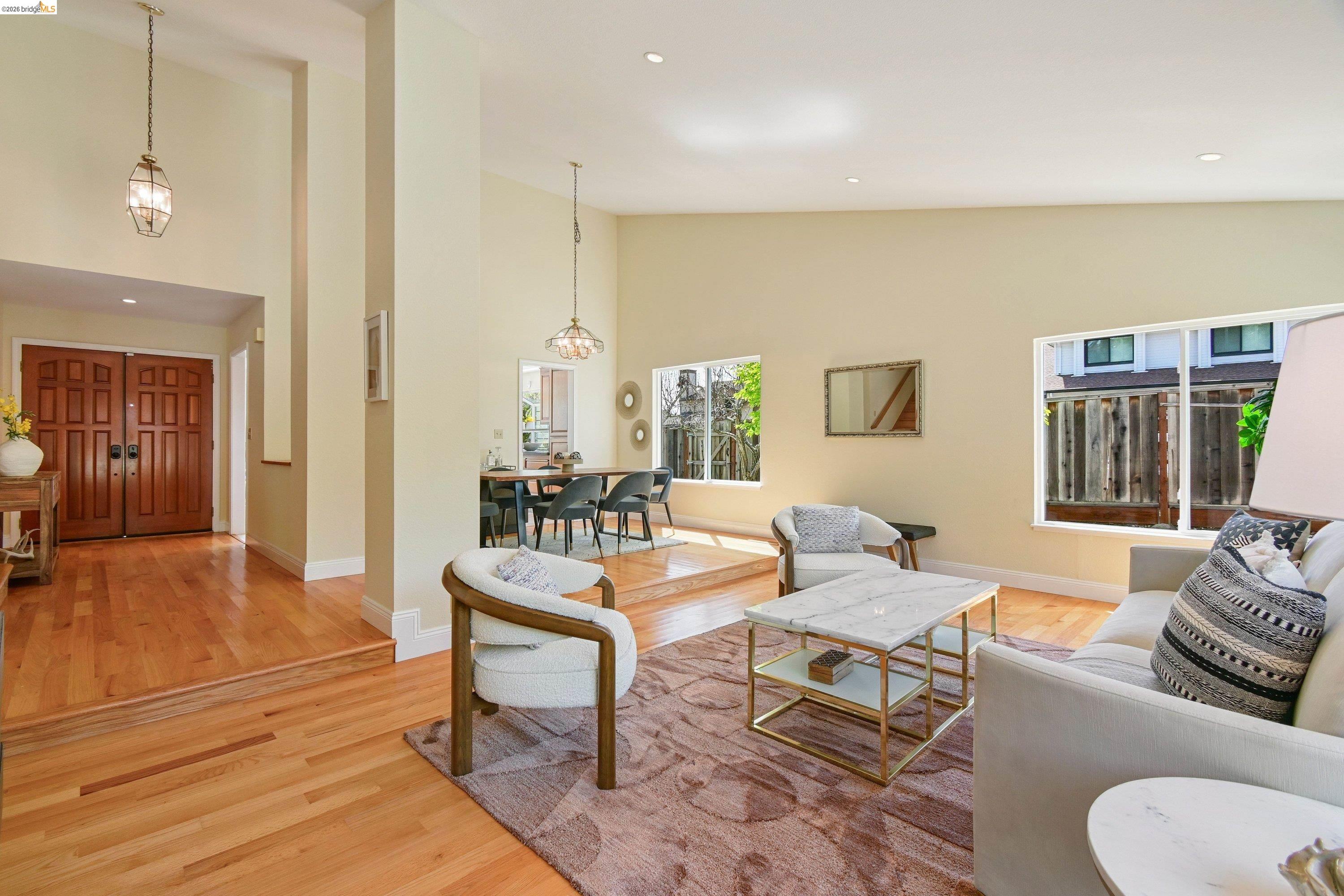 Light-filled living room with vaulted ceiling, oak floors, and a wide foyer view back to the double front doors