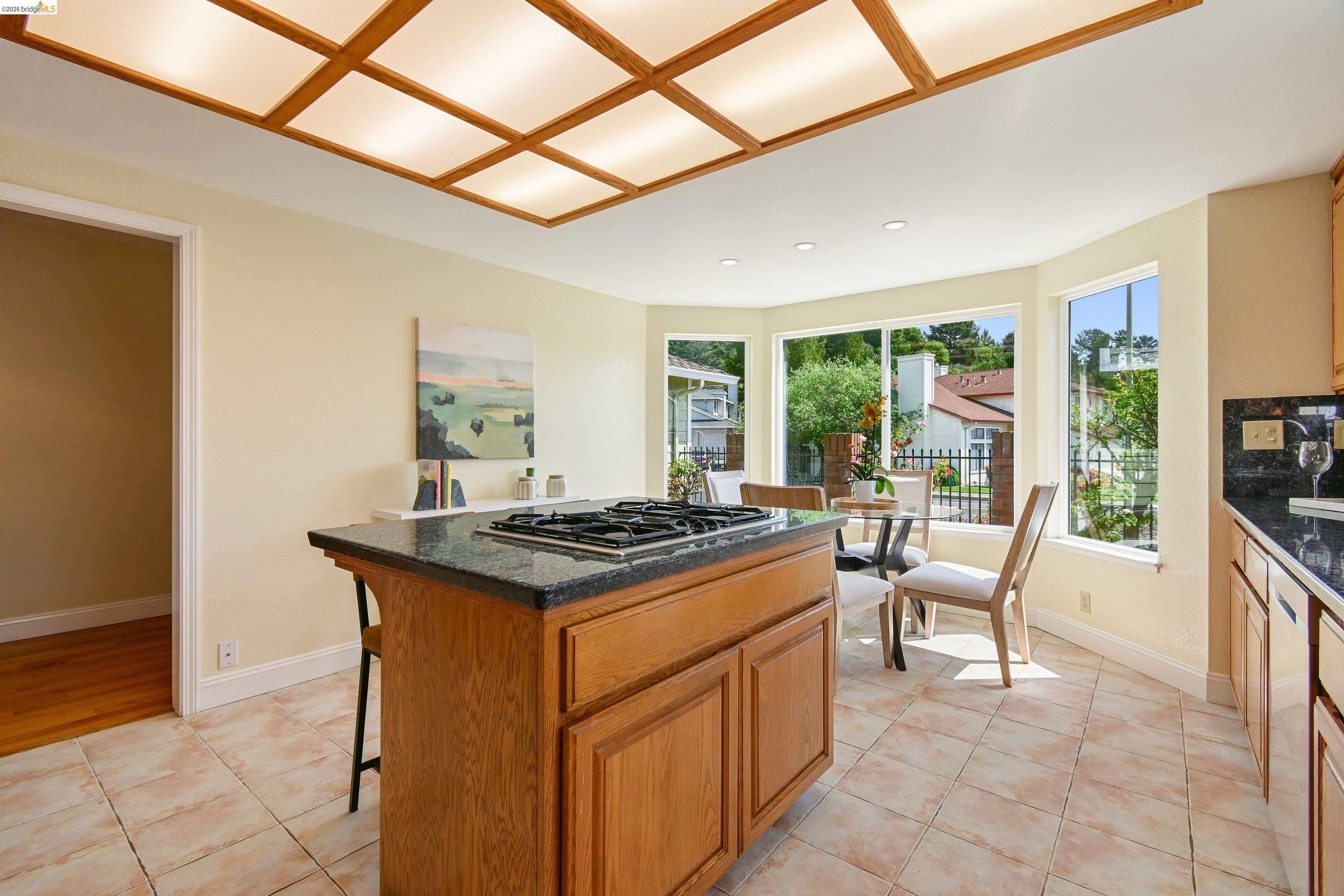 Eat-in kitchen island with gas cooktop, granite counters, oak cabinetry, and bay windows looking out to the neighborhood