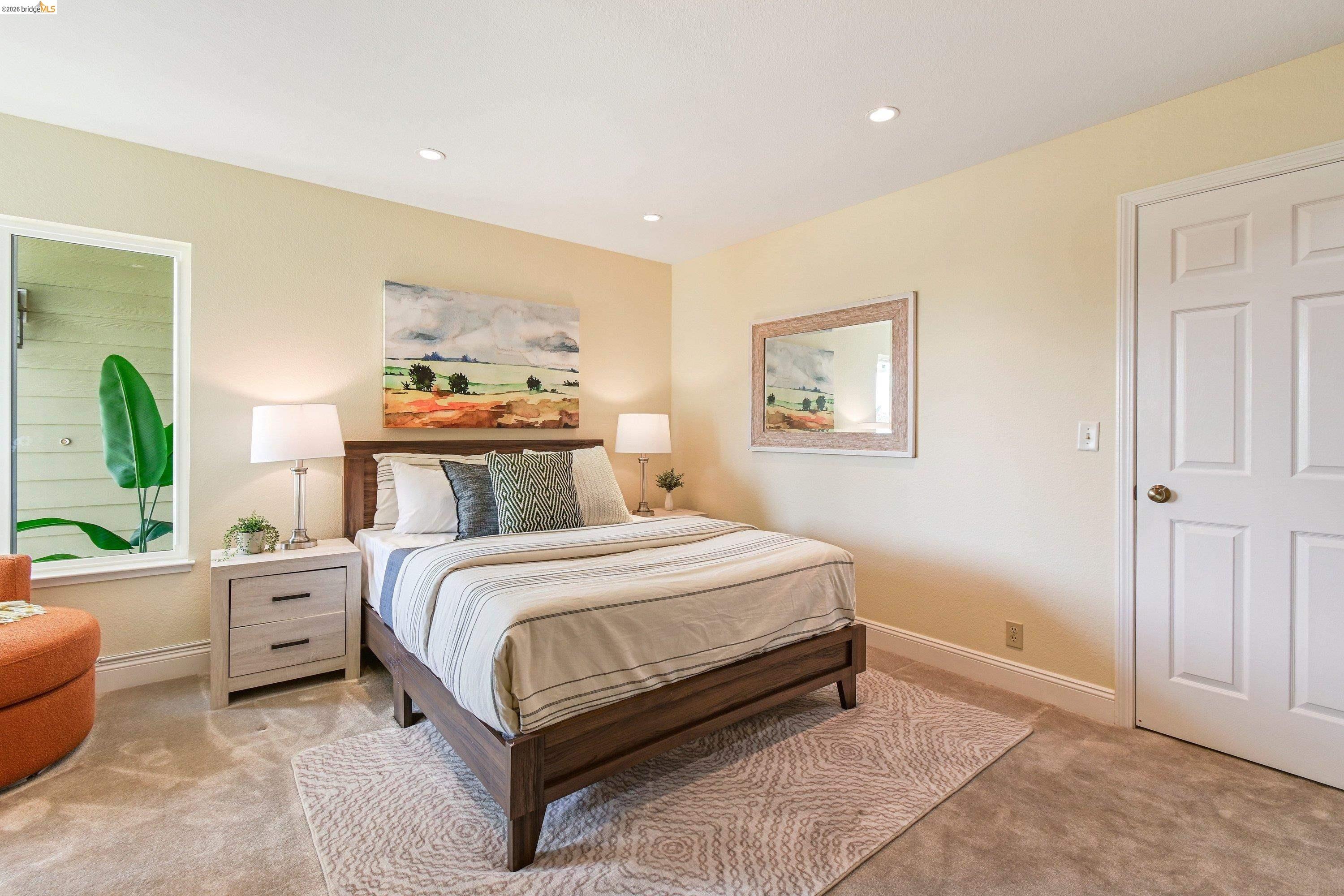 Primary suite with a wide king bed, soft butter-yellow walls, and dual closet doors leading to the en-suite bath